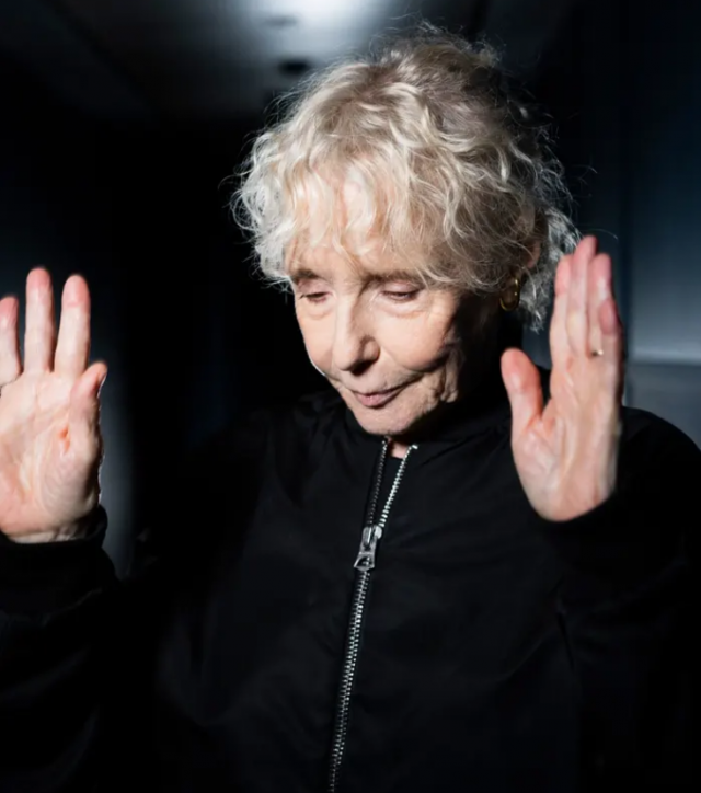 Claire Denis in a bomber jacket throwing her hands up